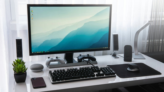 Bright white desk setup with a monitor, keyboard and a plant in daylight