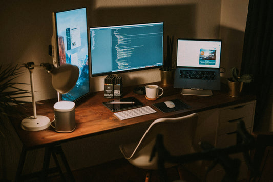 Wooden desk with two monitors, a desk lamp and cables running behind it