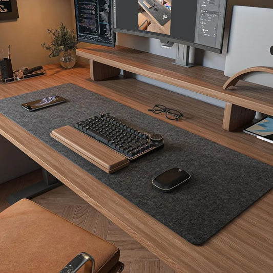 A tidy desk setup with a large felt desk mat, keyboard, monitor riser and a plant