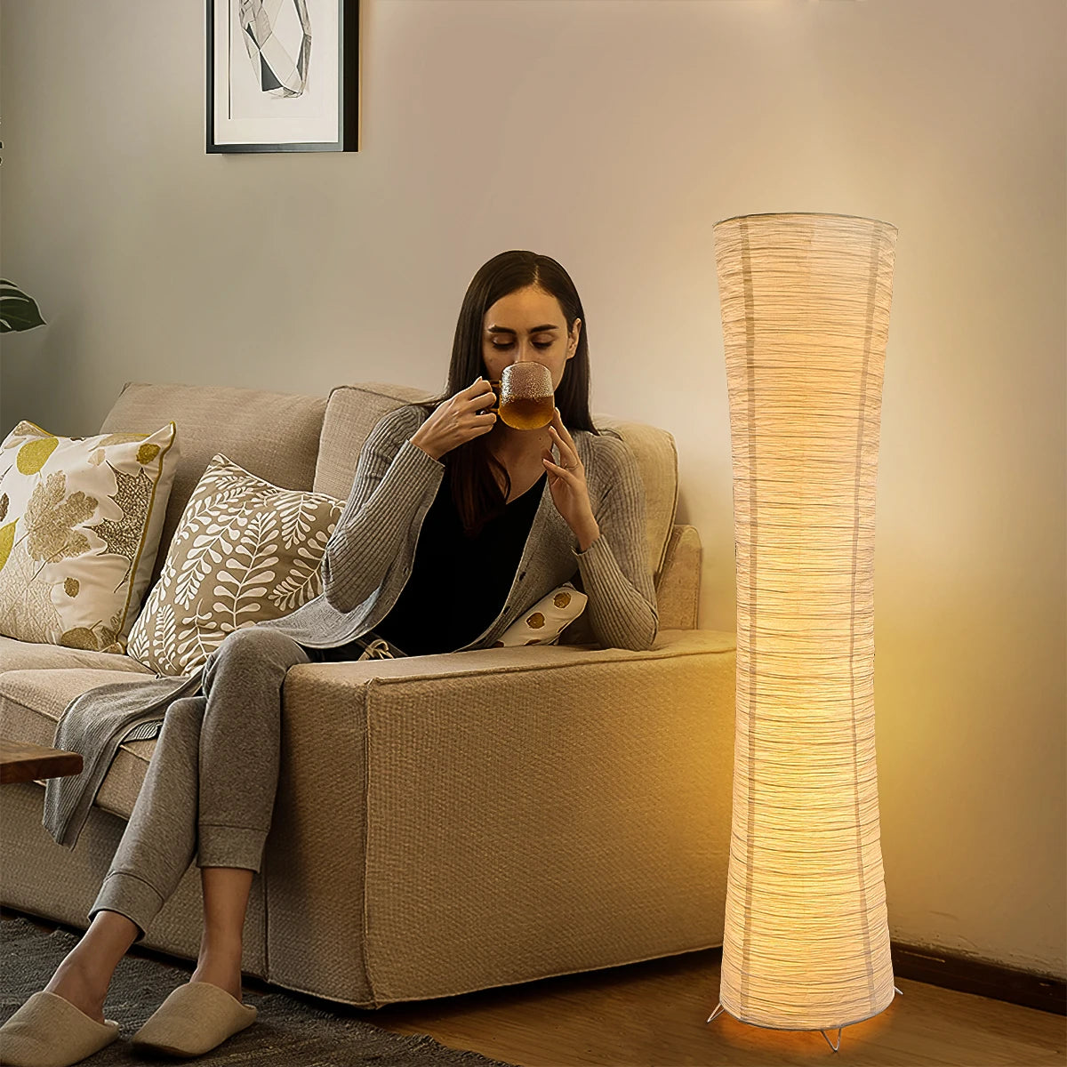 Woman sitting on a couch drinking from a glass in a cozy living room with a floor lamp.