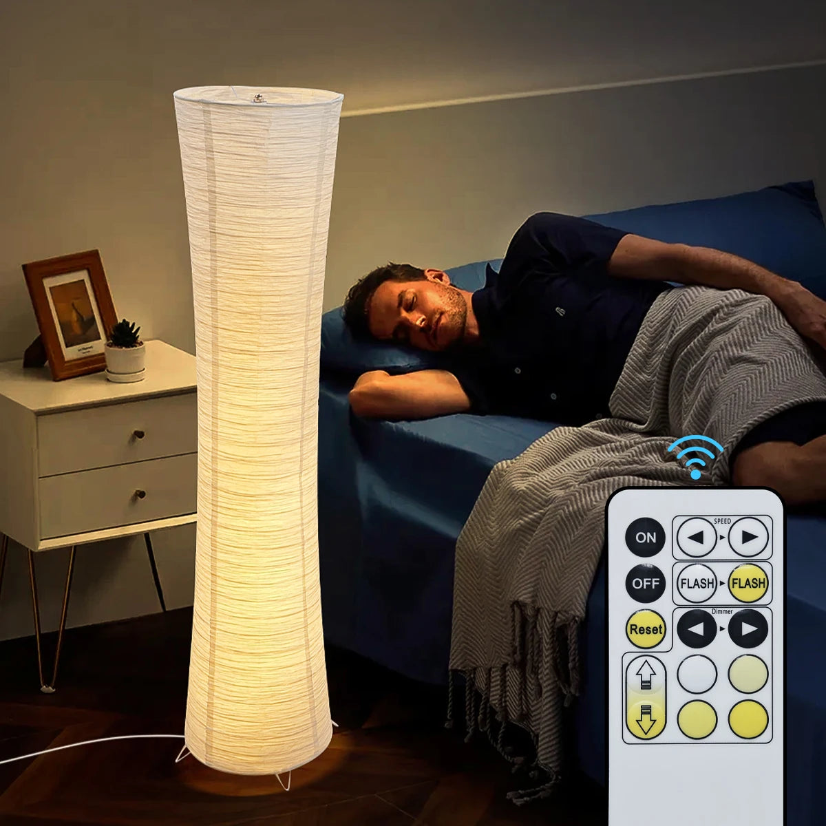 Man lying on a bed next to a tall floor lamp with a remote control in the foreground.