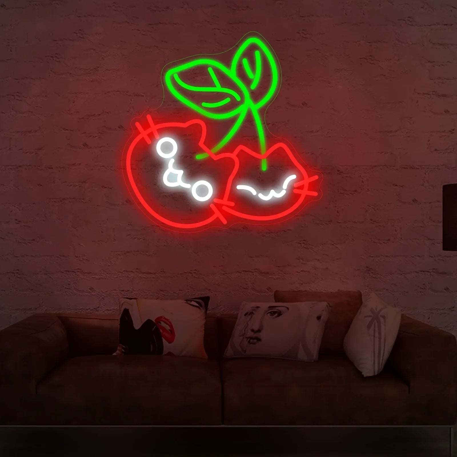 Neon sign of a cherries design on a brick wall above a couch with pillows.