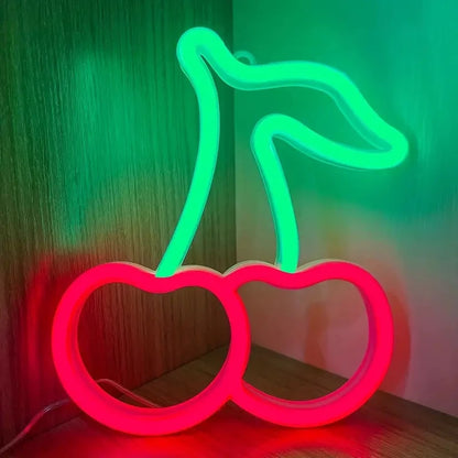 Neon light shaped like a cherry on a wooden surface with a green and pink gradient background.