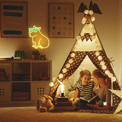 Children playing inside a lit teepee in a cozy room with a neon sign and bookshelf.